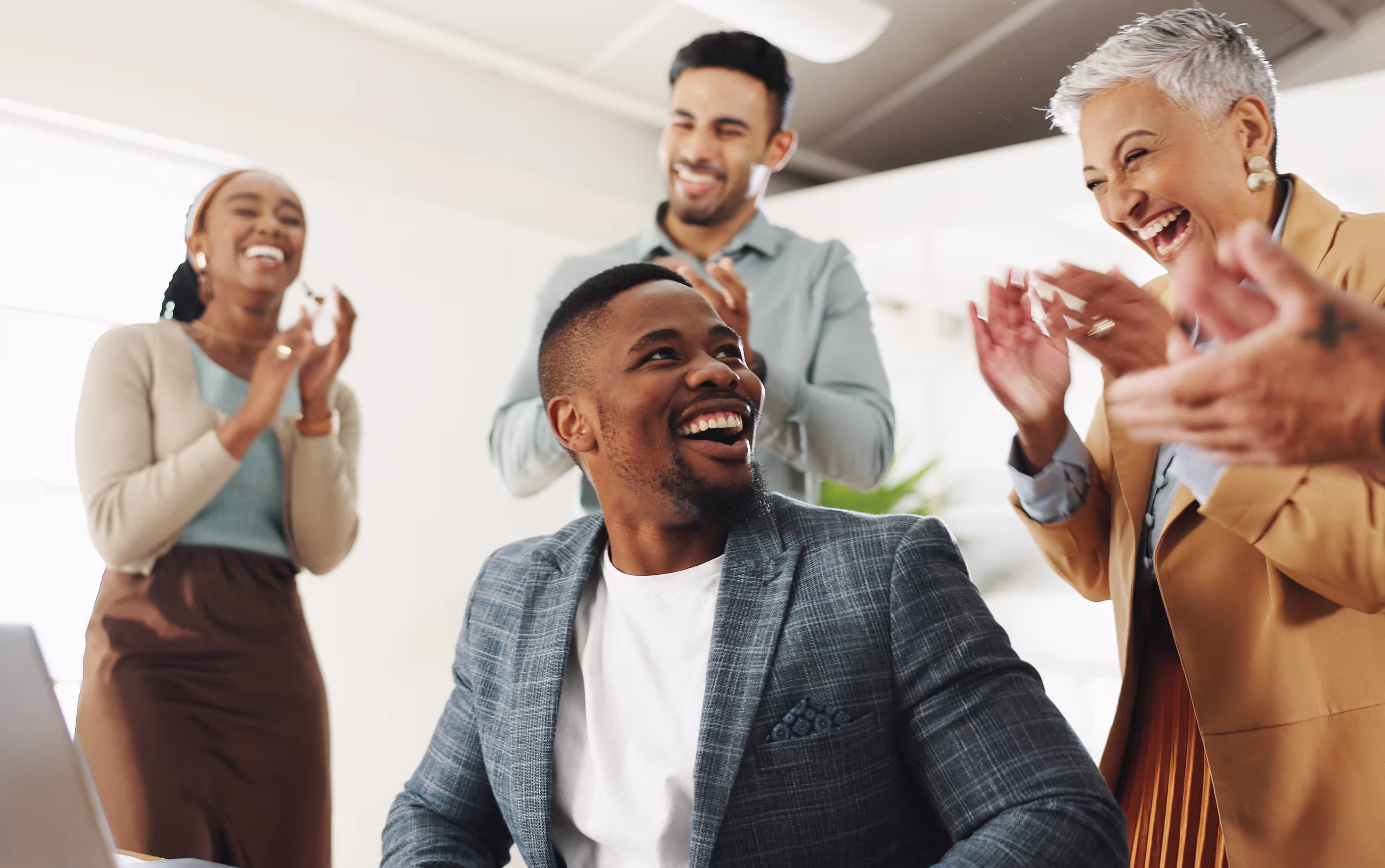Smiling diverse group of coworkers clapping and celebrating together in a bright office.
