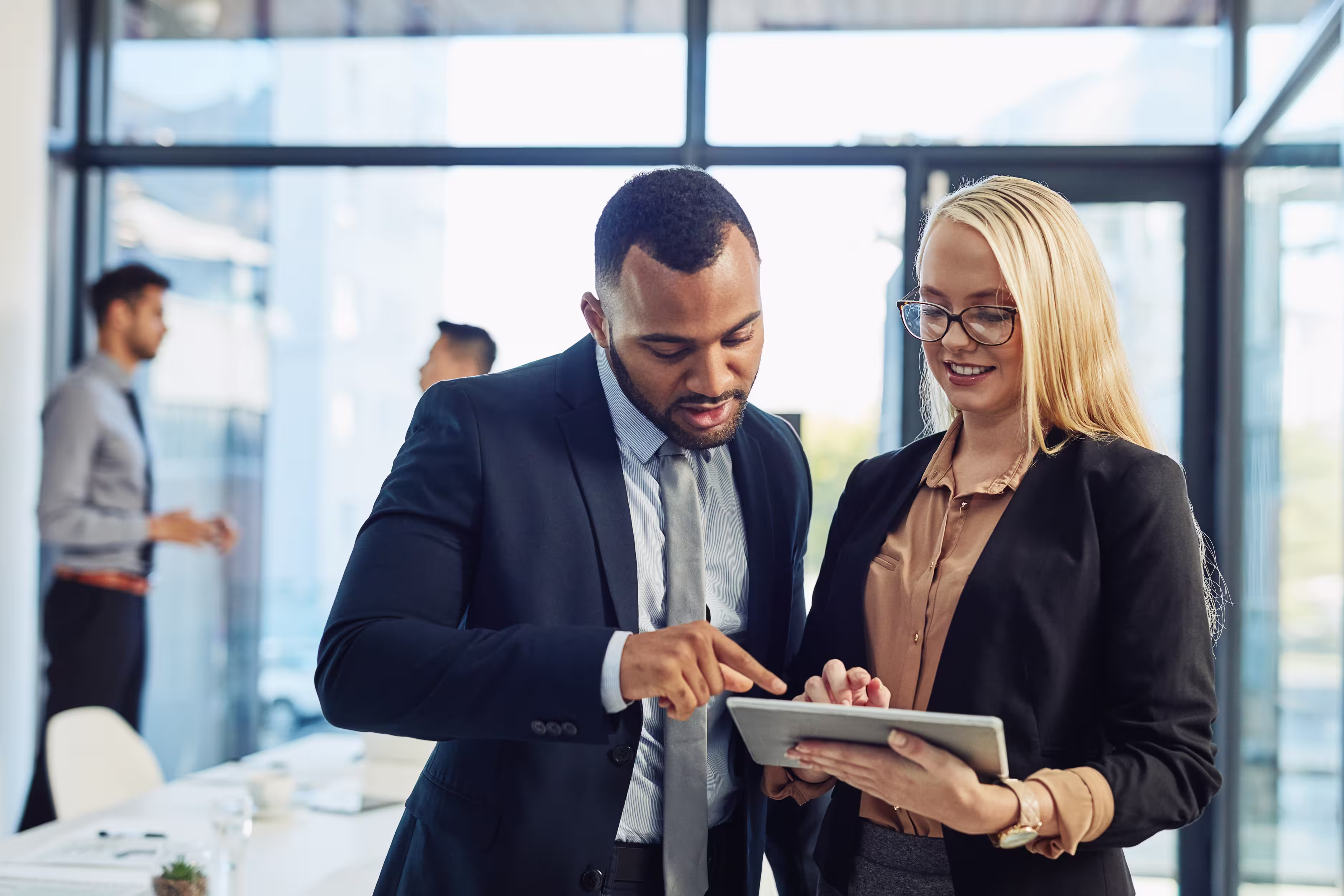 Two business professionals discussing work on a tablet in a modern office.