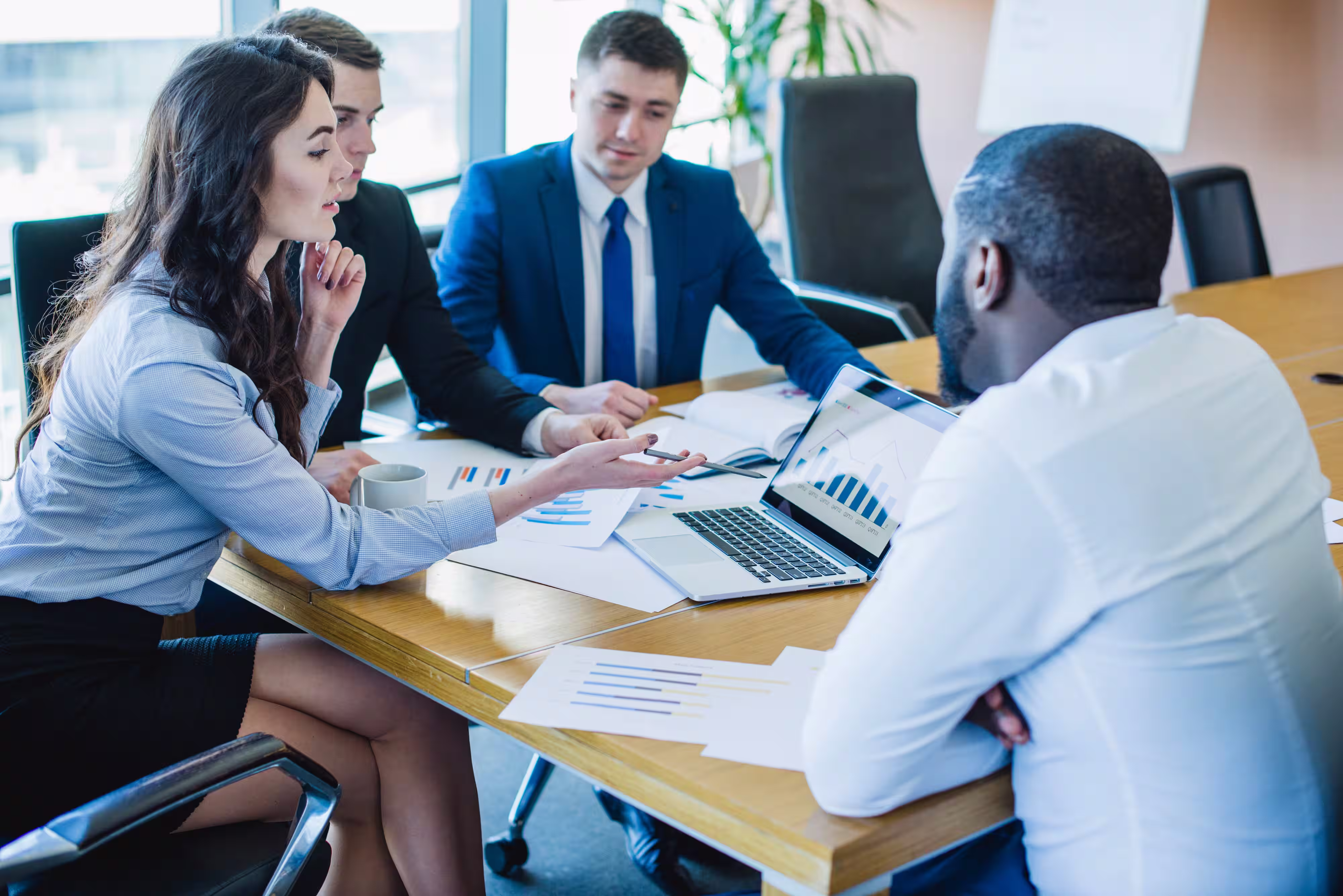 Four business professionals gathered around a conference table reviewing charts and graphs on papers and a laptop.