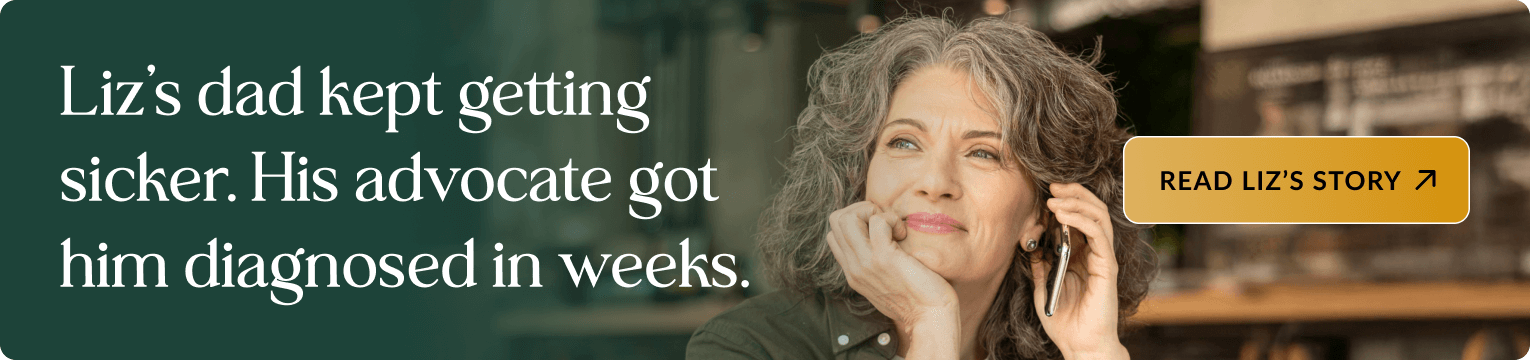 Middle-aged woman with curly gray hair wearing a dark green shirt, smiling while talking on a phone with her hand resting on her chin, in a modern kitchen with wooden shelving in the background. Banner text: Liz's dad kept getting sicker. His advocate got him diagnosed in weeks. Includes a button: READ LIZ'S STORY.
