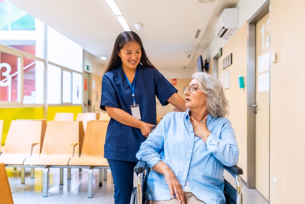 A senior woman being rolled in a wheelchair by a medical assistant.