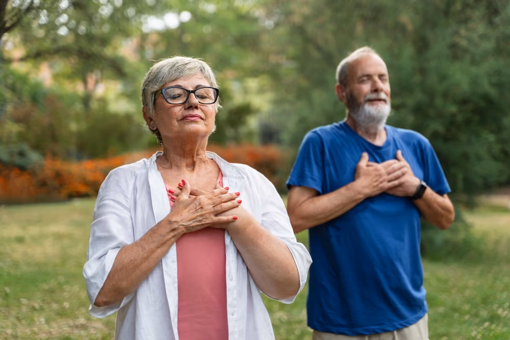 A woman and a man practice mindful breathing in a gentle nature setting.