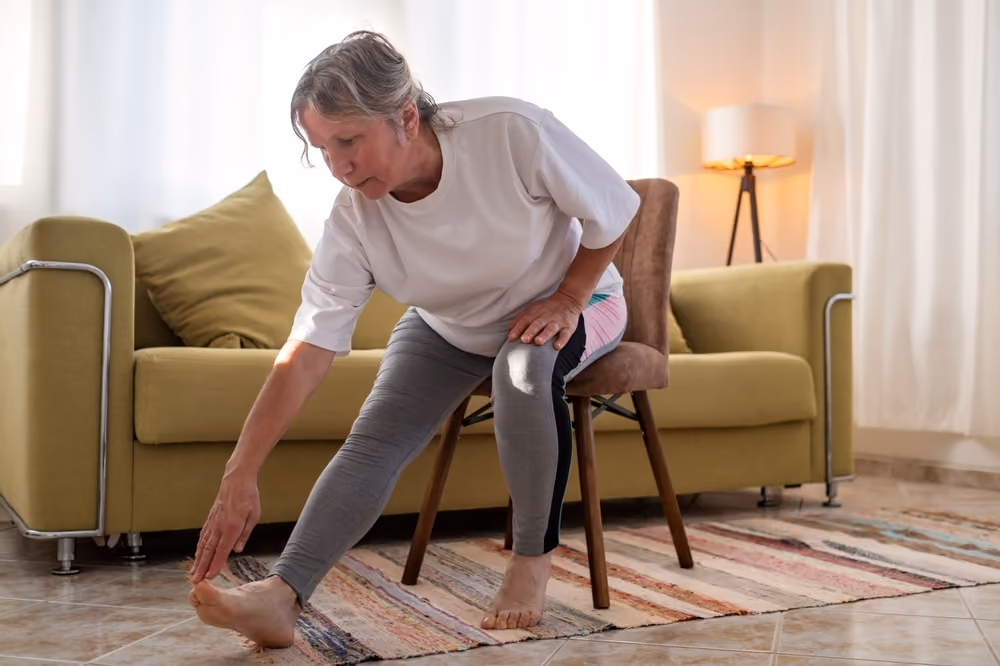 A senior woman, seated, stretching and touching her toes.