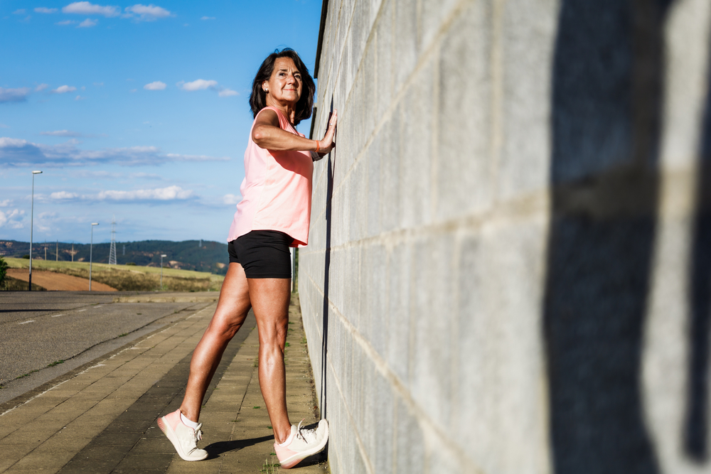 A woman performing a calf stretch against a wall.