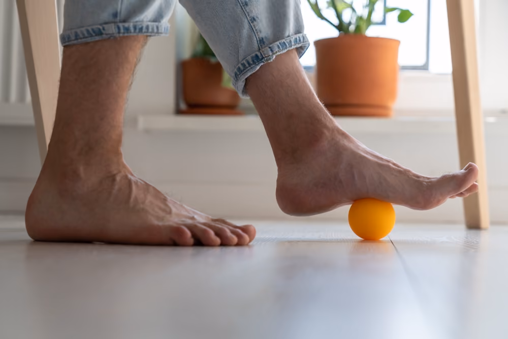A person performing foot rolls with a small rubber ball.