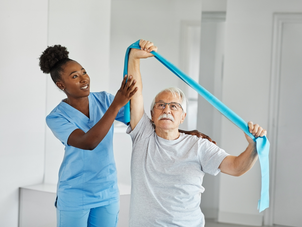 A man performing stretches with a health aide guiding them.