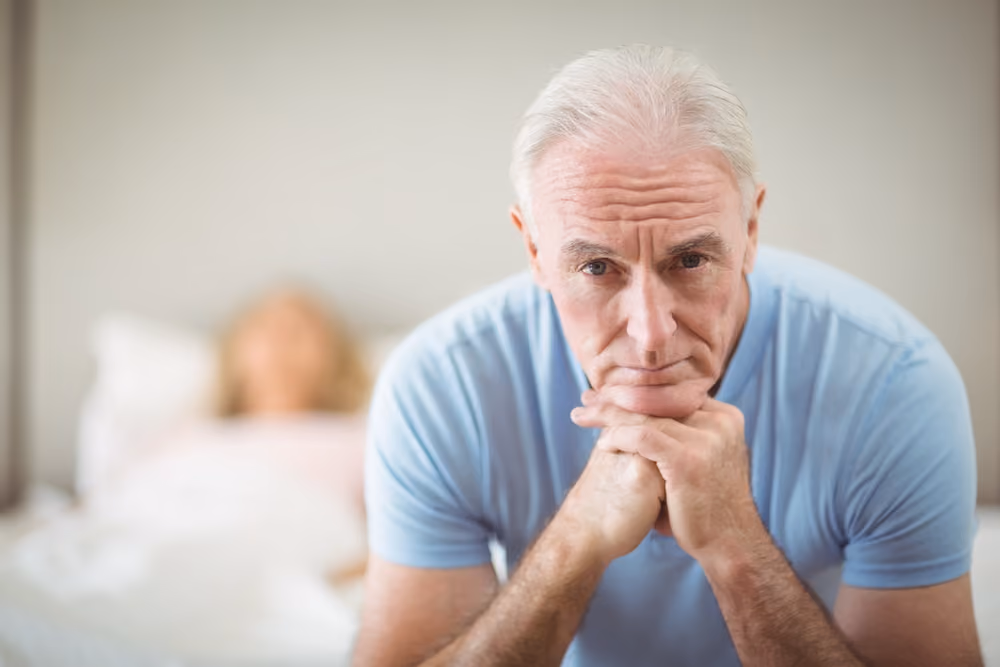 A depressed senior man sitting on his bed.