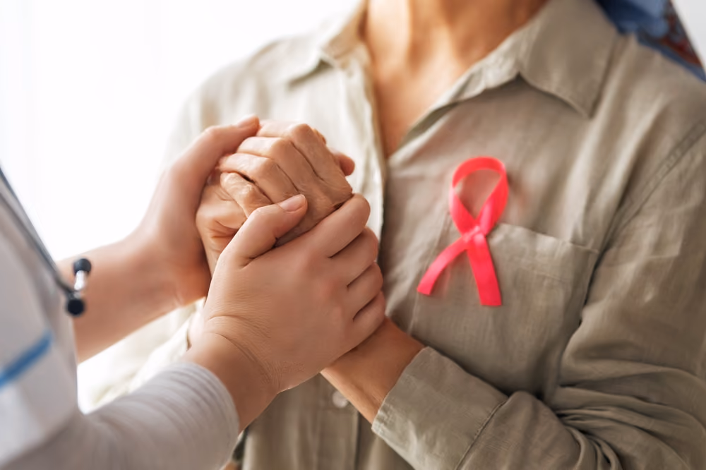 A doctor holding a woman;s hands while she's wearing a pink ribbon