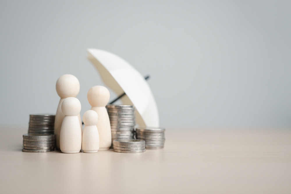 A wooden depiction of a family gathered under an umbrella with stacks of coins around them.