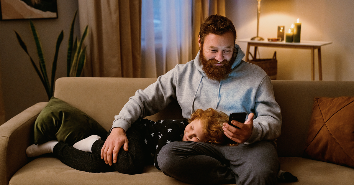 parent and child laying on the couch while parent is looking at mobile device
