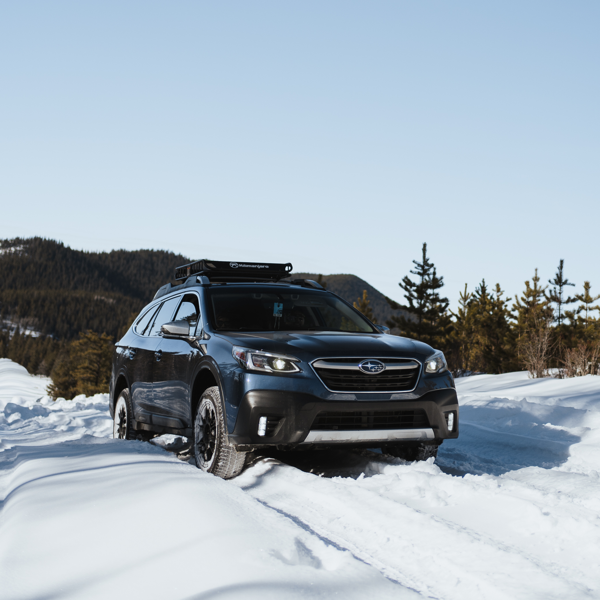 Modified Subaru Outback with roof rack driving through snow on a backcountry road in the Canadian Rockies