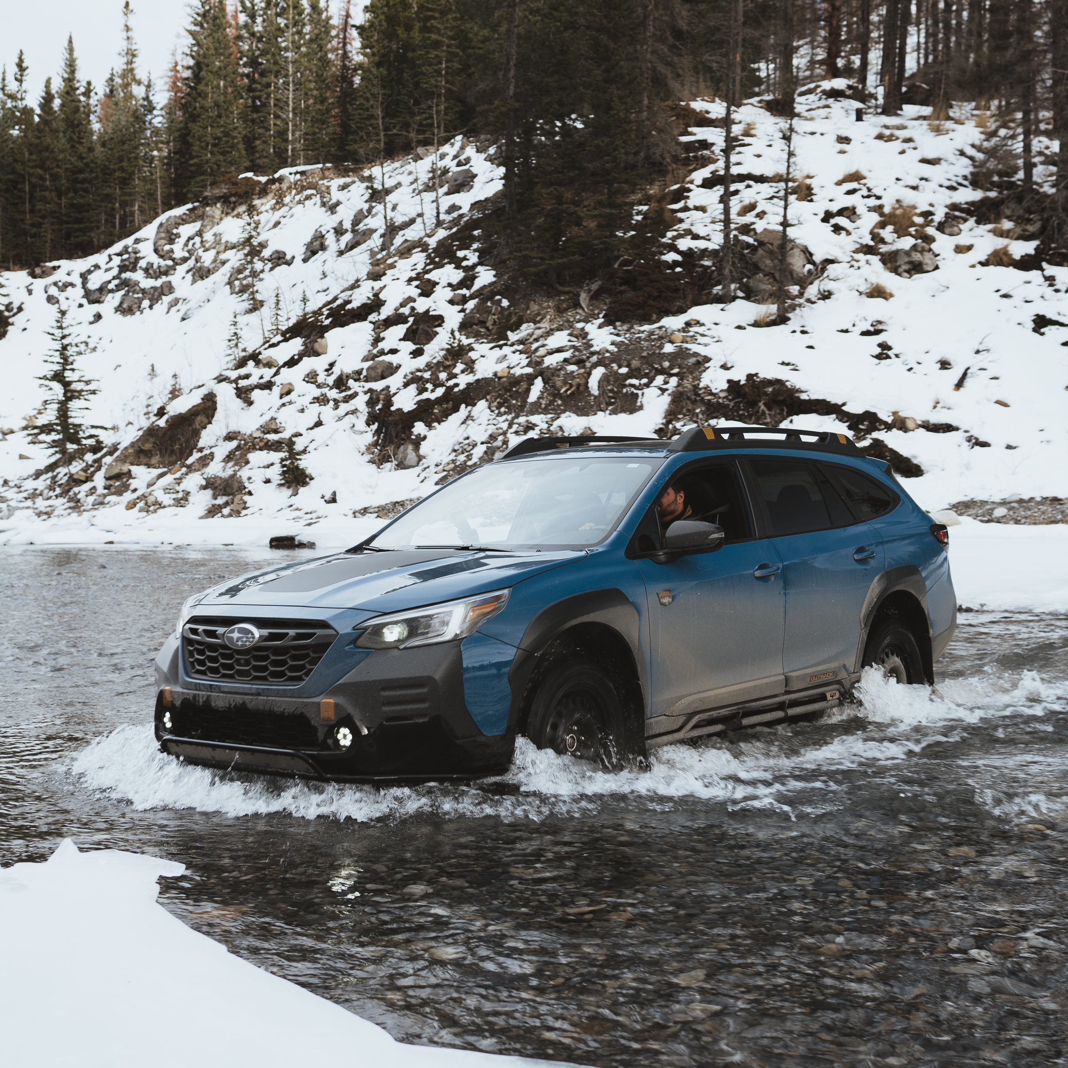 Modified Subaru Outback Wilderness with bumper guard fording a rocky river crossing in the Canadian Rockies