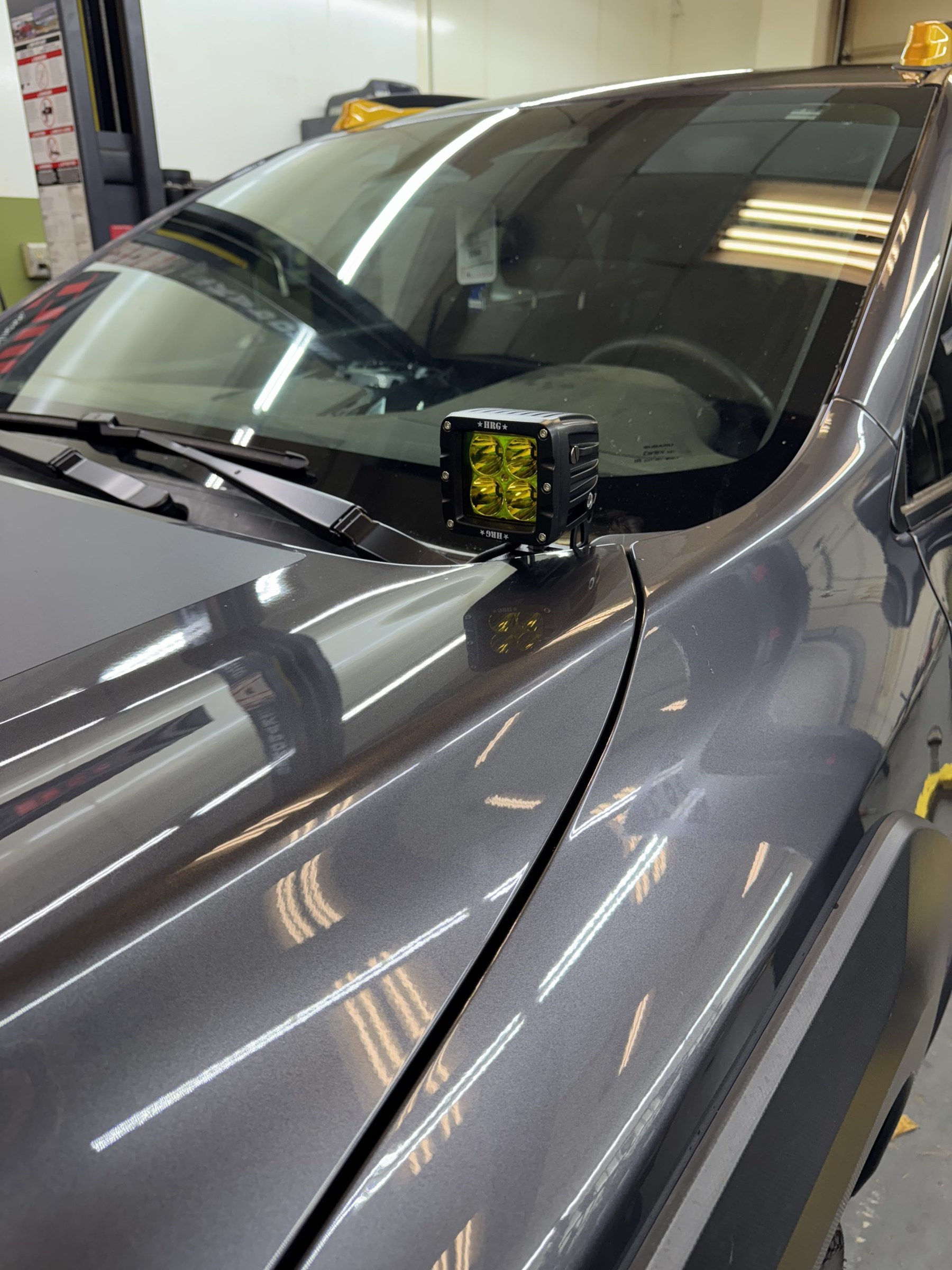 HRG Offroad ditch light bracket with a yellow pod light mounted at the hood hinge of a Subaru Crosstrek