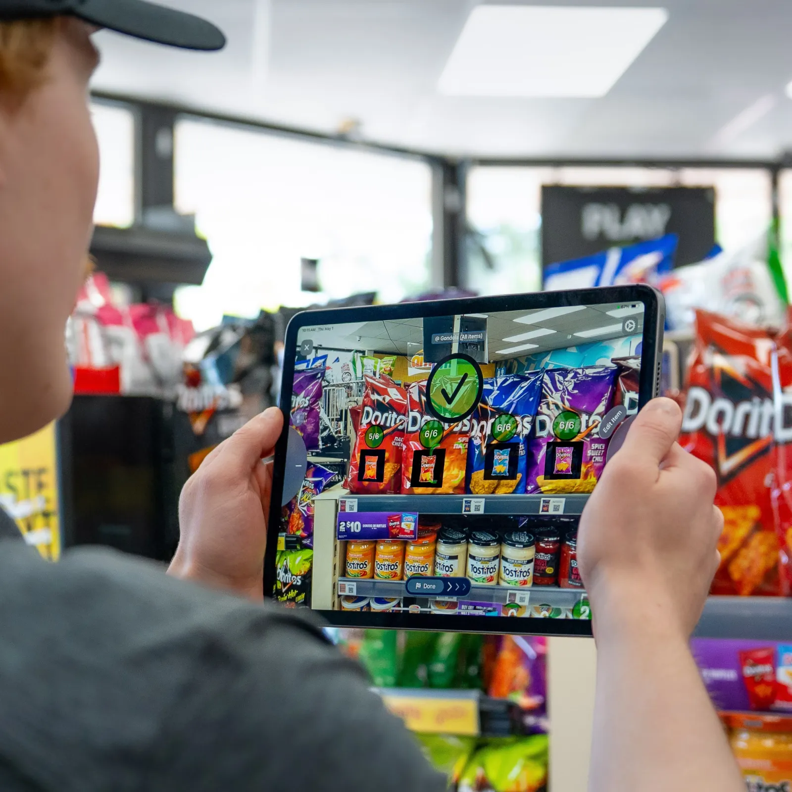 Man in a store using NomadGo on a tablet to scan the inventory level of bagged chips on a shelf.
