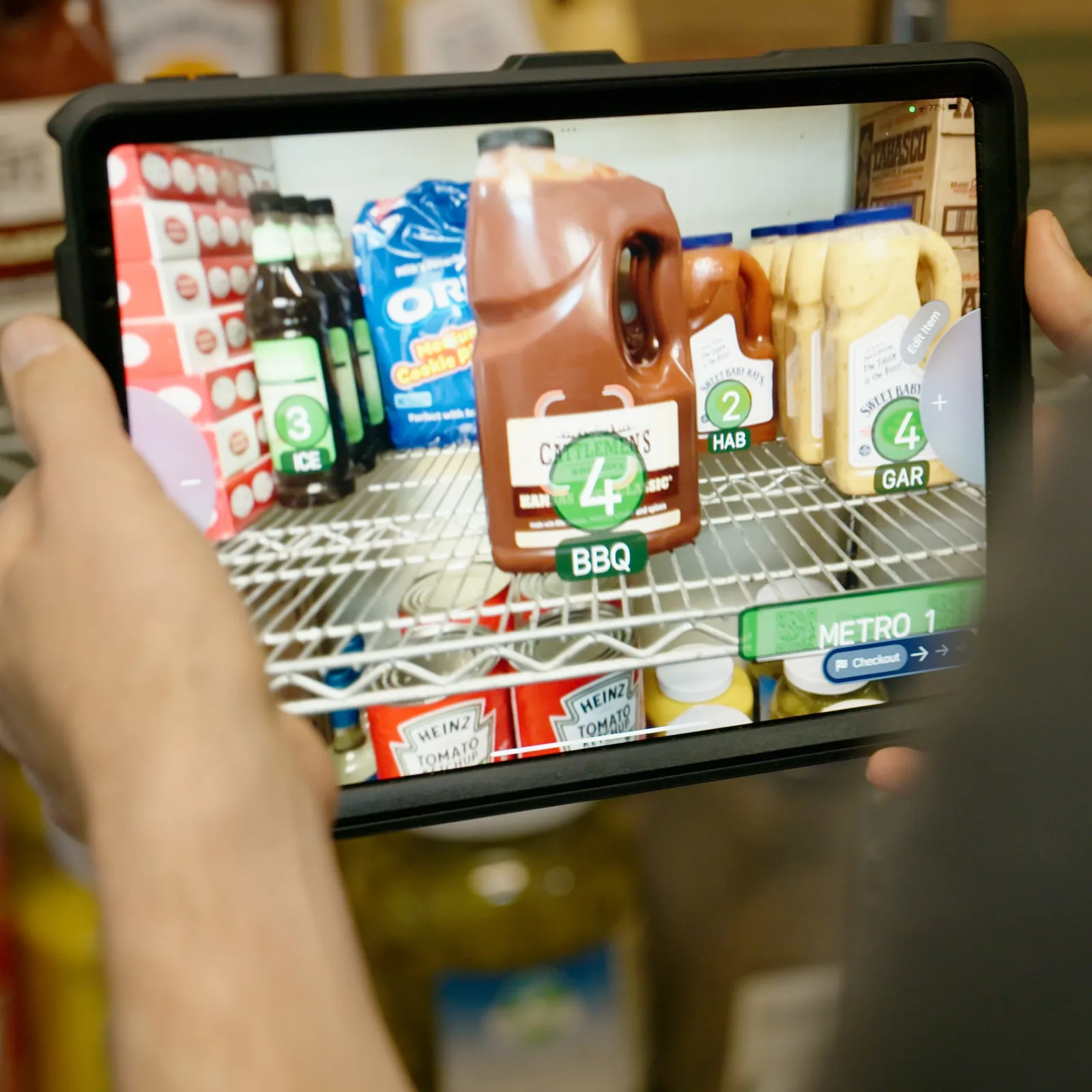Person holding a tablet scanning a large container of barbeque sauce on a metal rack shelf with NomadGo