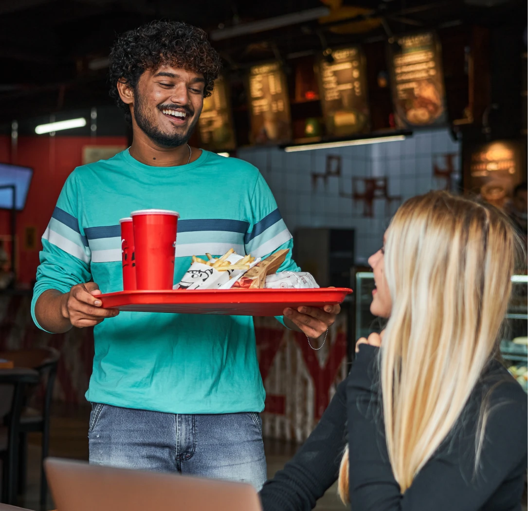 Man returning back to his table at a fast food restaurant holding a tray of food and a drink.
