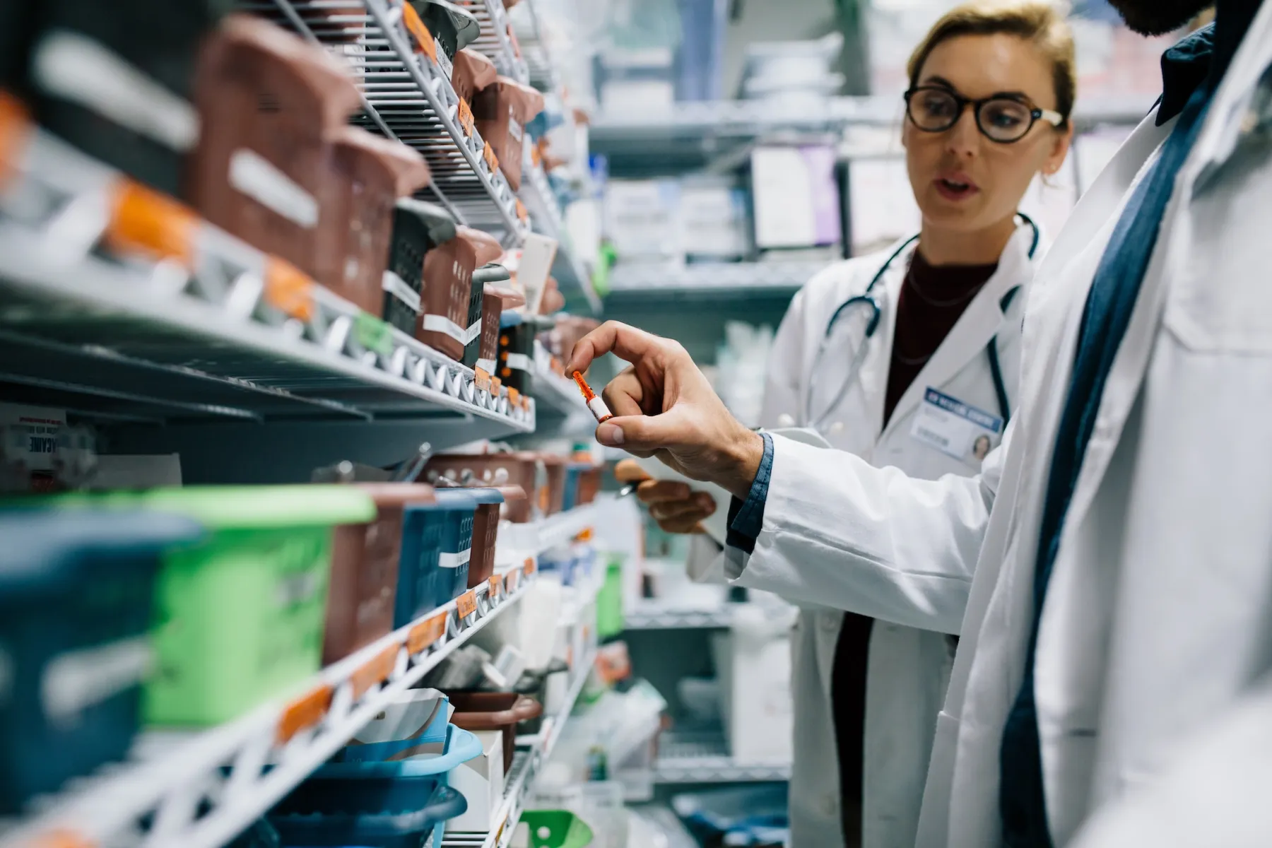 Two pharmacists in white coats selecting medication from shelves in a pharmacy.