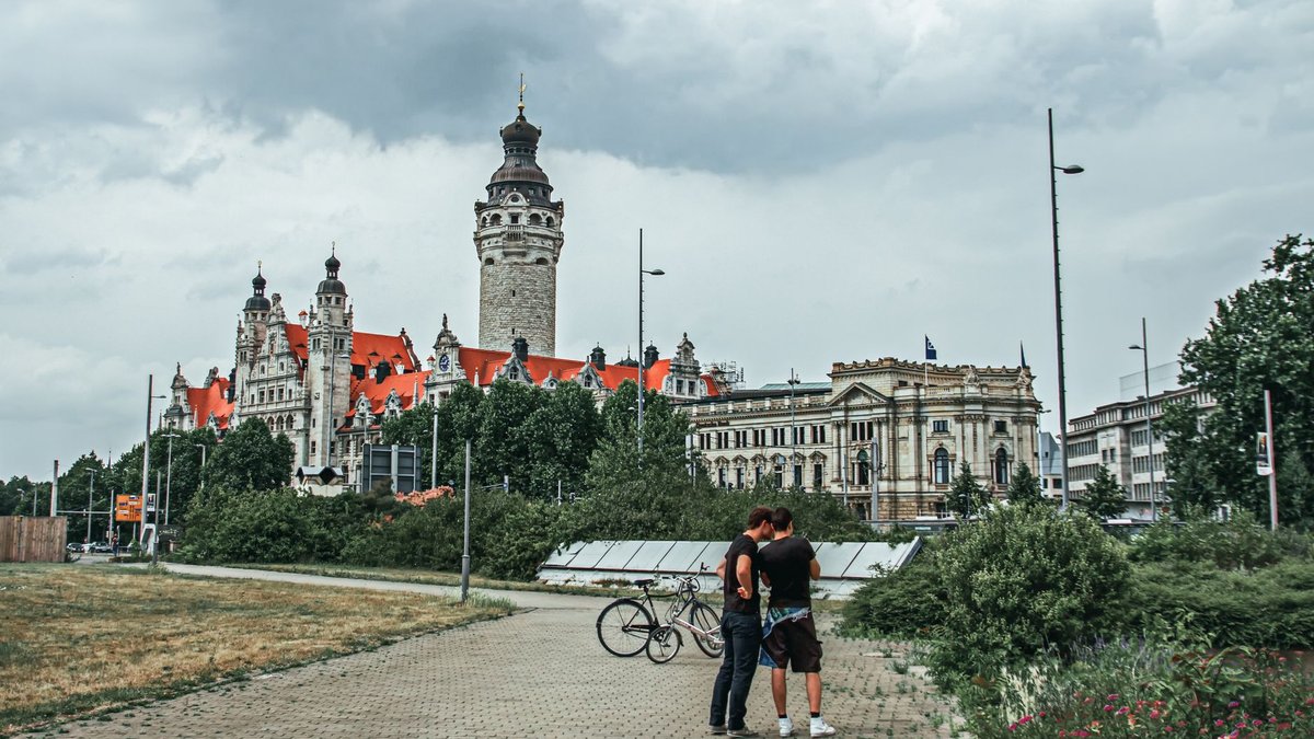 Zwei junge Leute mit Fahrrädern auf einem Weg in Leipzig, im Hintergrund das Neue Rathaus