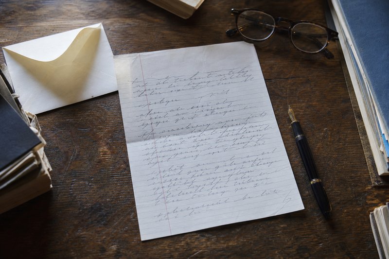 Handgeschriebenes Testament auf einem Holztisch, daneben ein Füllfederhalter, eine Lesebrille und ein geöffneter Umschlag