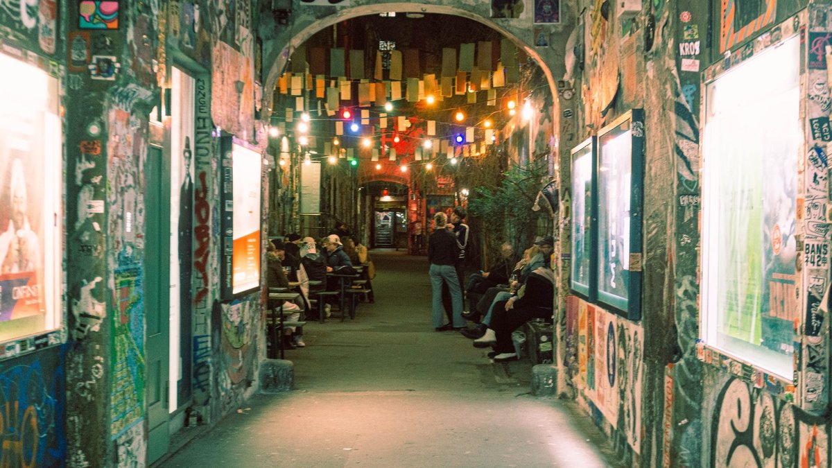 Beleuchteter Berliner Hinterhof am Abend mit Streetart an den Wänden und Menschen vor einer Bar
