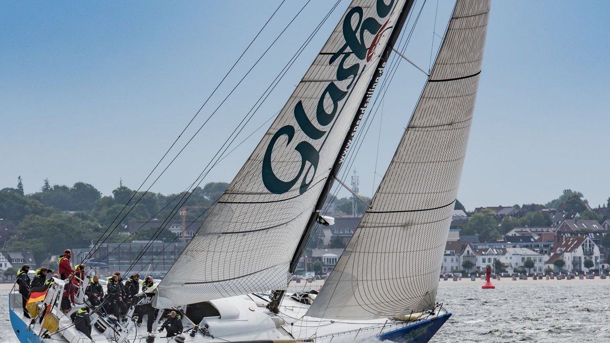 Regattayacht mit ausgerittener Crew auf der Kieler Förde, dahinter die Küste