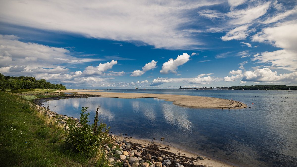 Sandbank und Steinstrand an der Kieler Förde, dahinter Segelboote auf der Ostsee