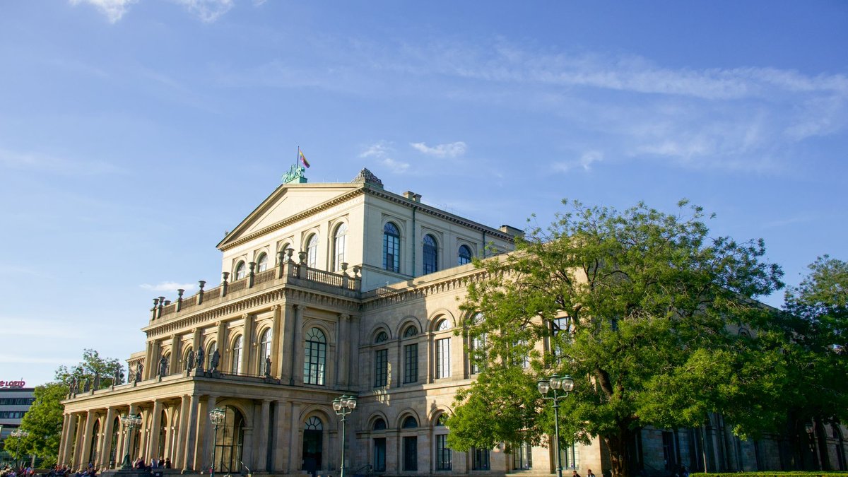 Das klassizistische Opernhaus in Hannover im Abendlicht, davor sitzen Menschen auf den Stufen