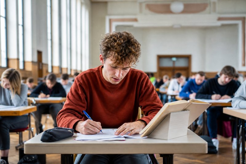 Student schreibt im Prüfungssaal handschriftlich an einer Examensklausur