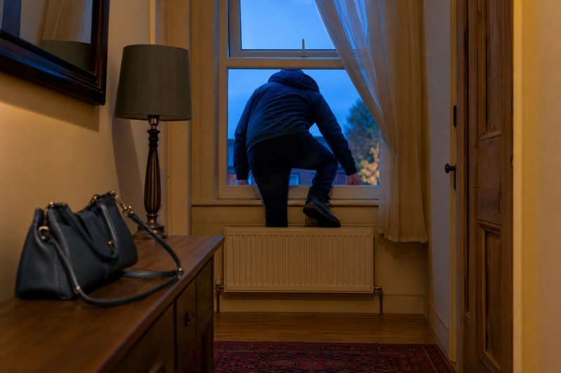 Person steigt in der Dämmerung durch ein gekipptes Fenster in eine Wohnung
