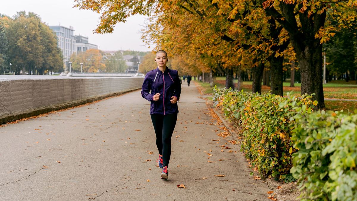 Läuferin joggt auf einem Uferweg zwischen herbstlichen Bäumen