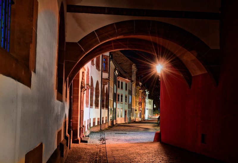 Beleuchteter Torbogen und Kopfsteinpflastergasse in der Freiburger Altstadt bei Nacht