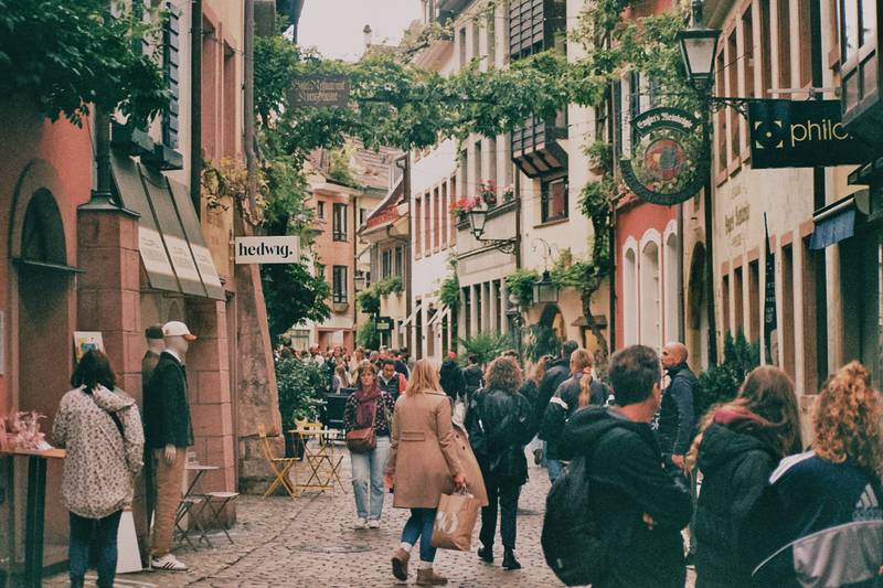 Belebte Kopfsteinpflastergasse in der Freiburger Altstadt mit Cafés und Passanten