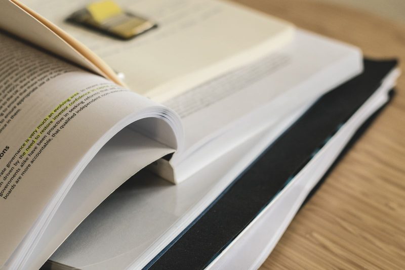 Mehrere aufgeschlagene Bücher liegen übereinander gestapelt auf einem Tisch