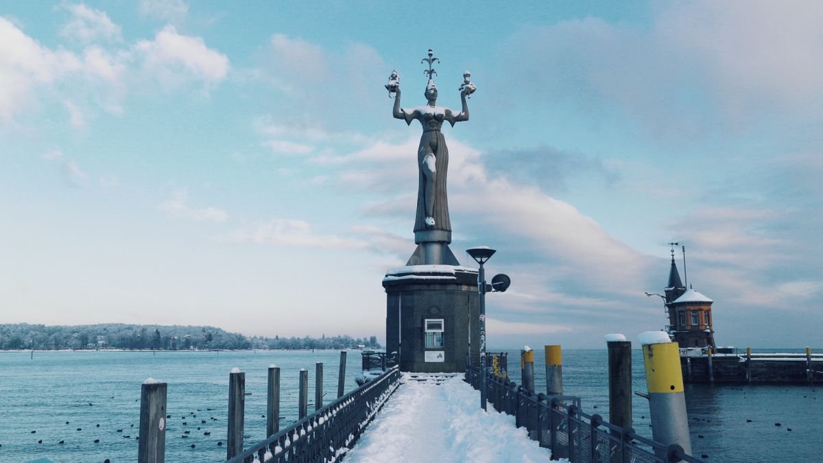Die Imperia-Statue an der Hafeneinfahrt von Konstanz im Winter, dahinter der Bodensee
