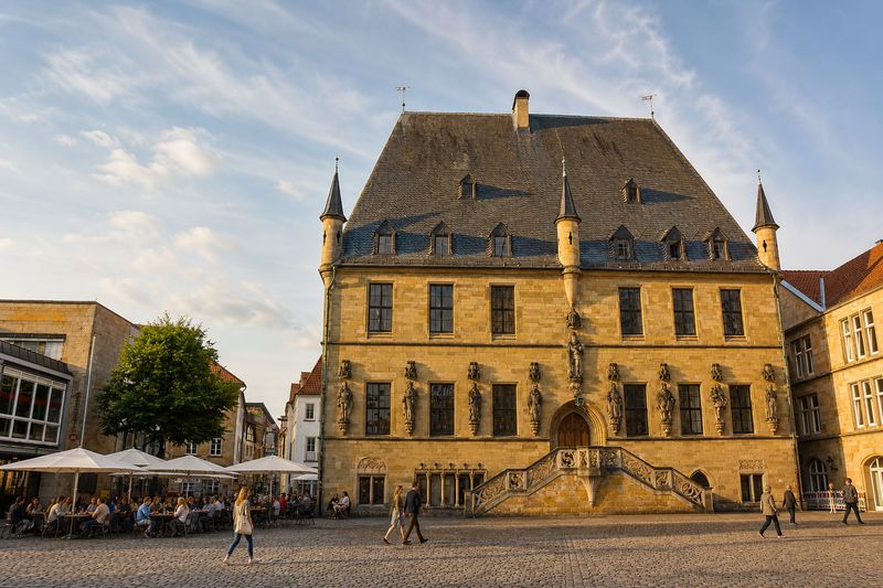 Das historische Rathaus am Markt in Osnabrück im Abendlicht, davor Cafétische und Passanten