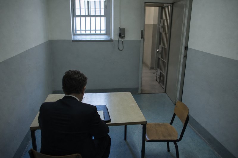 Anwalt sitzt mit Akte im kargen Besuchsraum einer Justizvollzugsanstalt und wartet auf seinen Mandanten