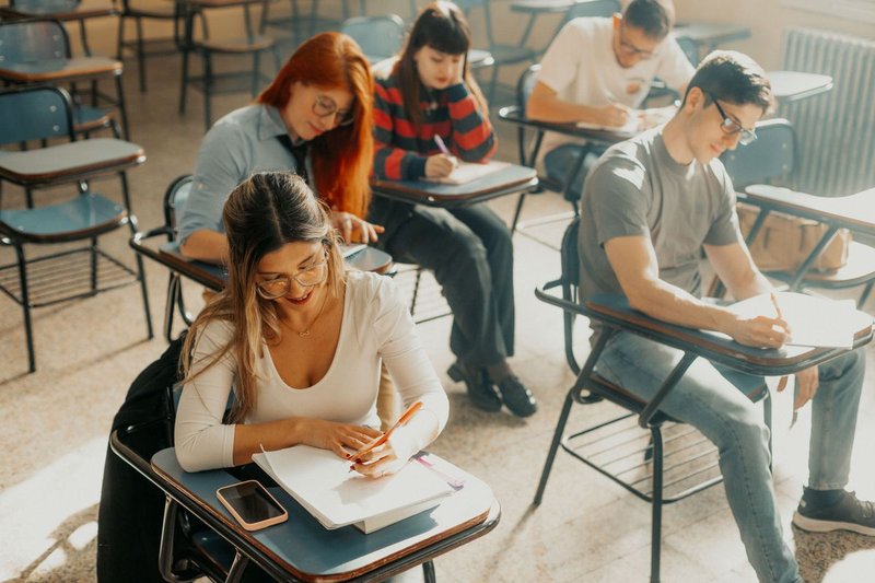 Studierende sitzen an Einzeltischen in einem hellen Seminarraum und schreiben eine Klausur