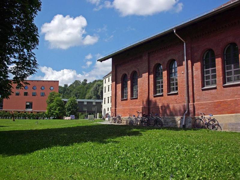 Backsteingebäude und Campuswiese der Universität Passau an der Innpromenade, davor abgestellte Fahrräder
