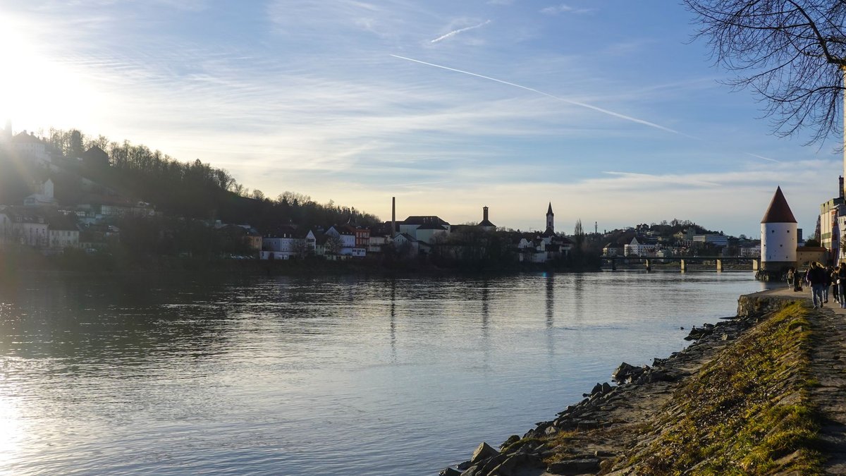 Sonnenaufgang über dem Flussufer in Passau, die Häuser spiegeln sich im ruhigen Wasser