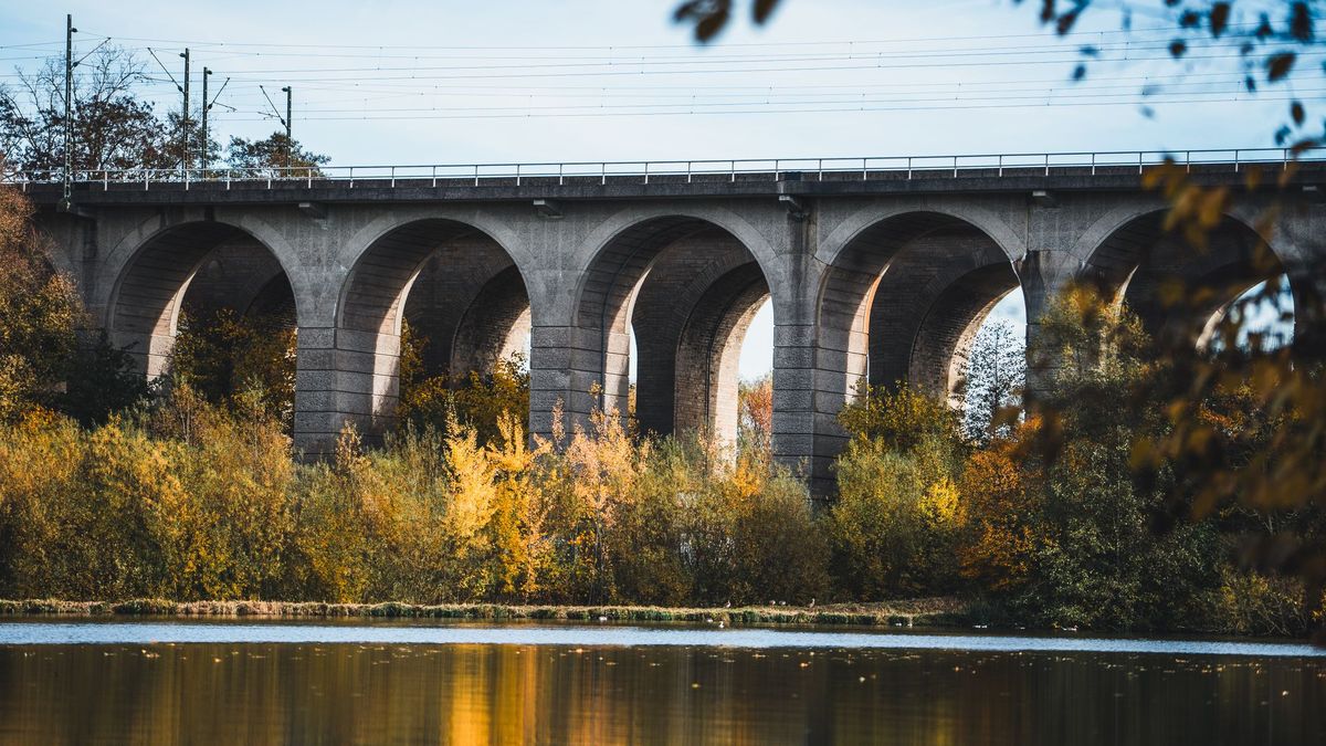 Eisenbahnbrücke in Bielefeld über einem Fluss, umgeben von herbstlich gefärbten Bäumen