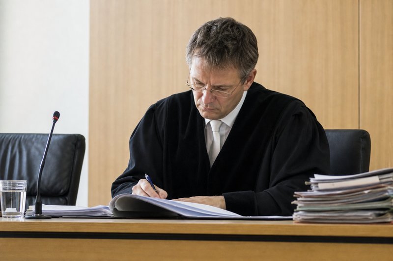 Ein Richter in schwarzer Robe beugt sich über eine offene Akte und macht sich eine Notiz