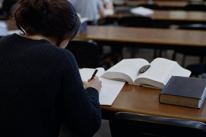 Studentin schreibt in der Klausur von Hand, daneben liegt ein aufgeschlagener Gesetzestext