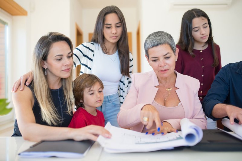 Drei Generationen sitzen mit Immobilienunterlagen an einem Tisch und besprechen sie