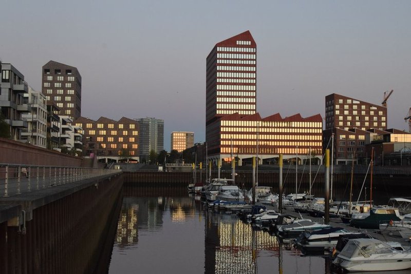 Moderne Gebäude am Wasser in der Bremer Überseestadt im Abendlicht, davor liegen Boote