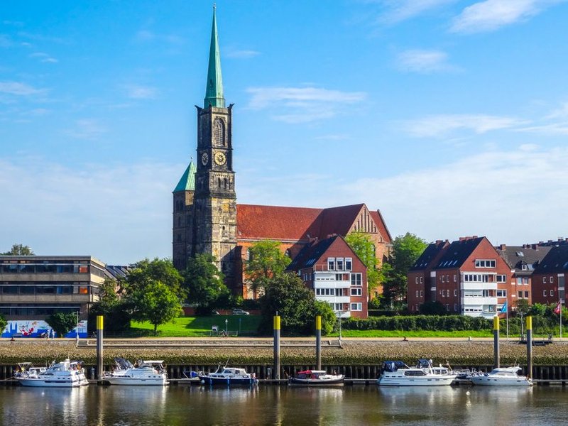 Kirche St. Stephani über dem Weserufer in Bremen, davor ein Bootsanleger