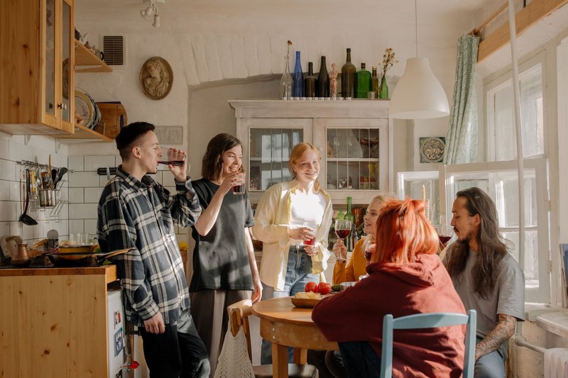 Sechs junge Leute stehen und sitzen mit Getränken in einer Küche zusammen und unterhalten sich