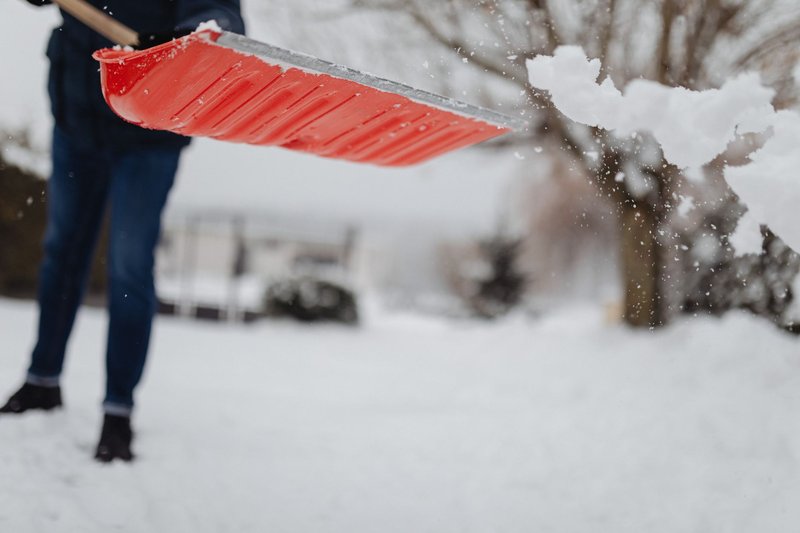 Person räumt mit einer roten Schneeschaufel einen verschneiten Weg