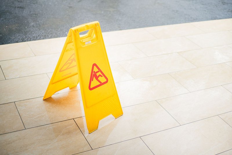 Gelbes Warnschild für nassen Boden steht auf hellen Fliesen in einem Eingangsbereich