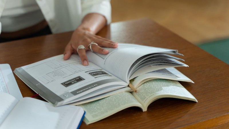 Hände blättern an einem Holztisch in mehreren aufgeschlagenen Büchern