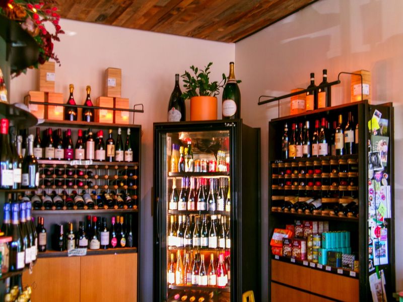 Innenraum einer Weinhandlung mit gefüllten Regalen und einem beleuchteten Kühlschrank voller Flaschen